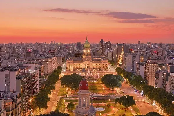 Aerial view of a city skyline at sunset, with a lit historic building and orange-pink sky.