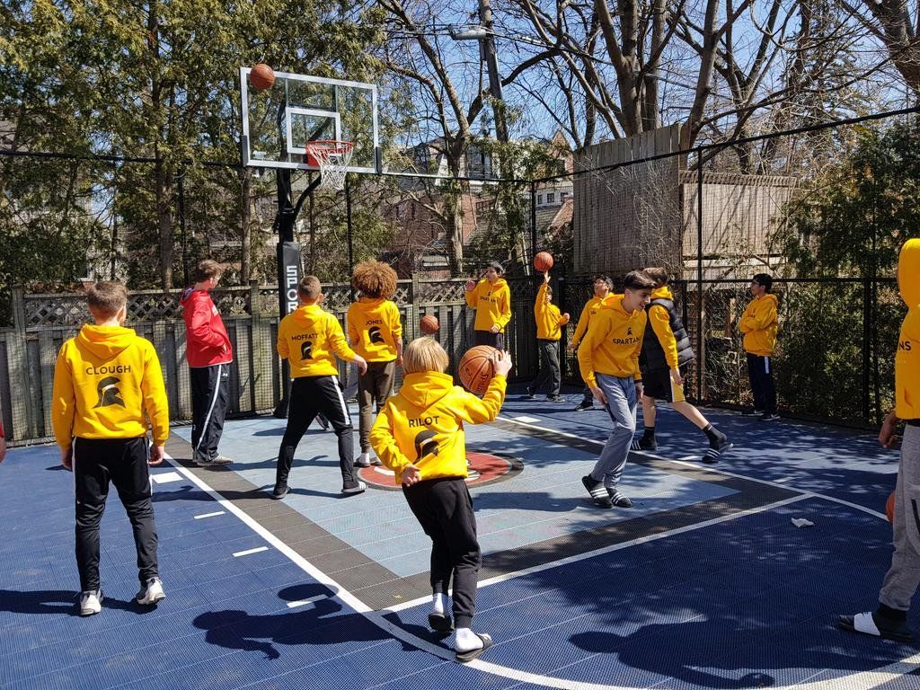People playing basketball on an outdoor court in yellow jerseys, with a hoop and trees in the background
