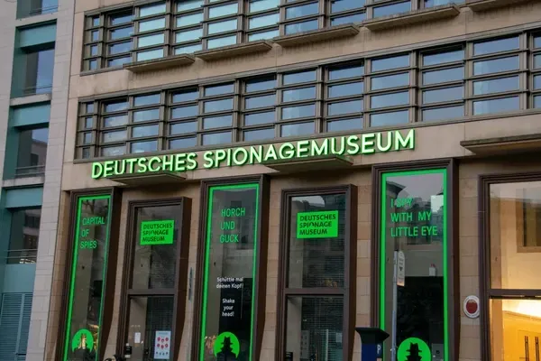 Entrance to the Deutsches Spionagemuseum, with green neon signage and glass doors on a city street.