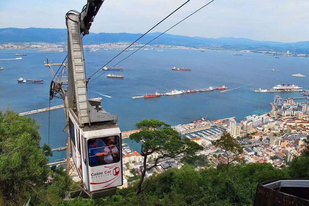 Cable car descending over a coastal bay with boats and a city skyline in the distance