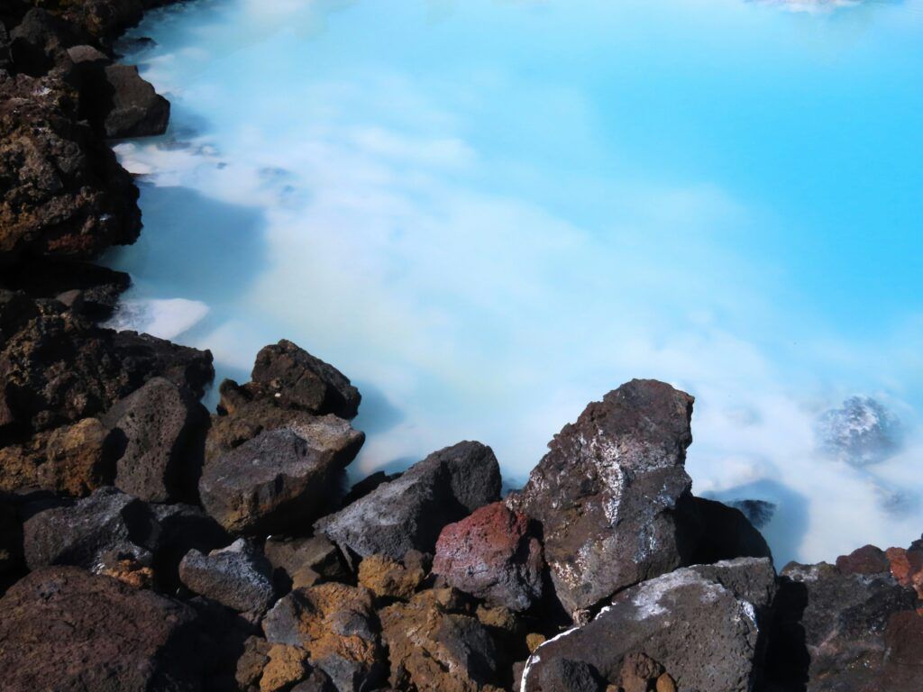 Rocky shoreline beside bright turquoise water with white foam