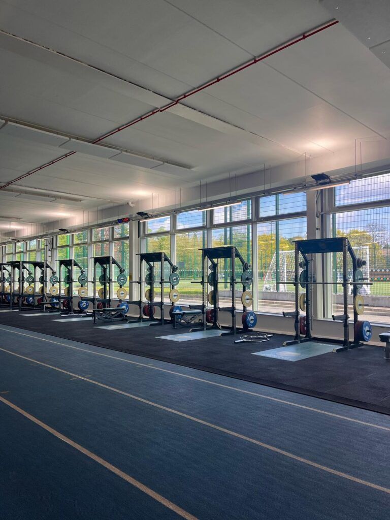Indoor gym with treadmill rows beside large windows and a blue running track