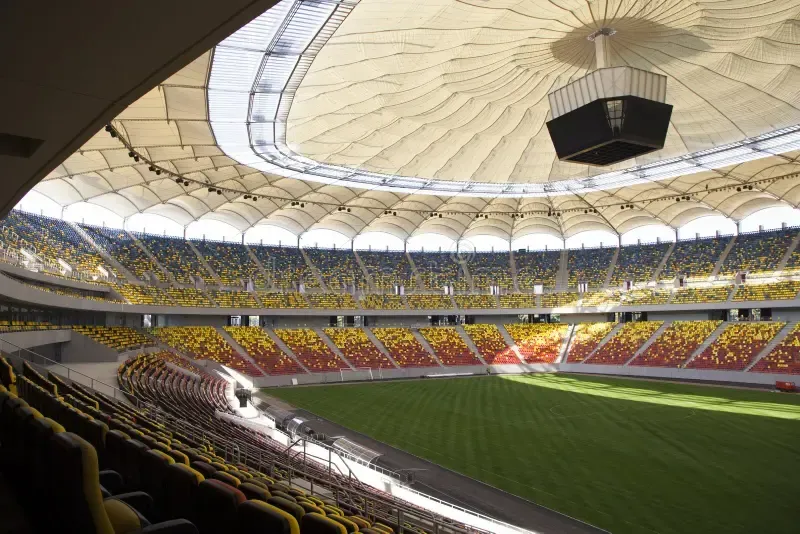 Empty stadium with yellow and red seats and a green field under a large domed roof
