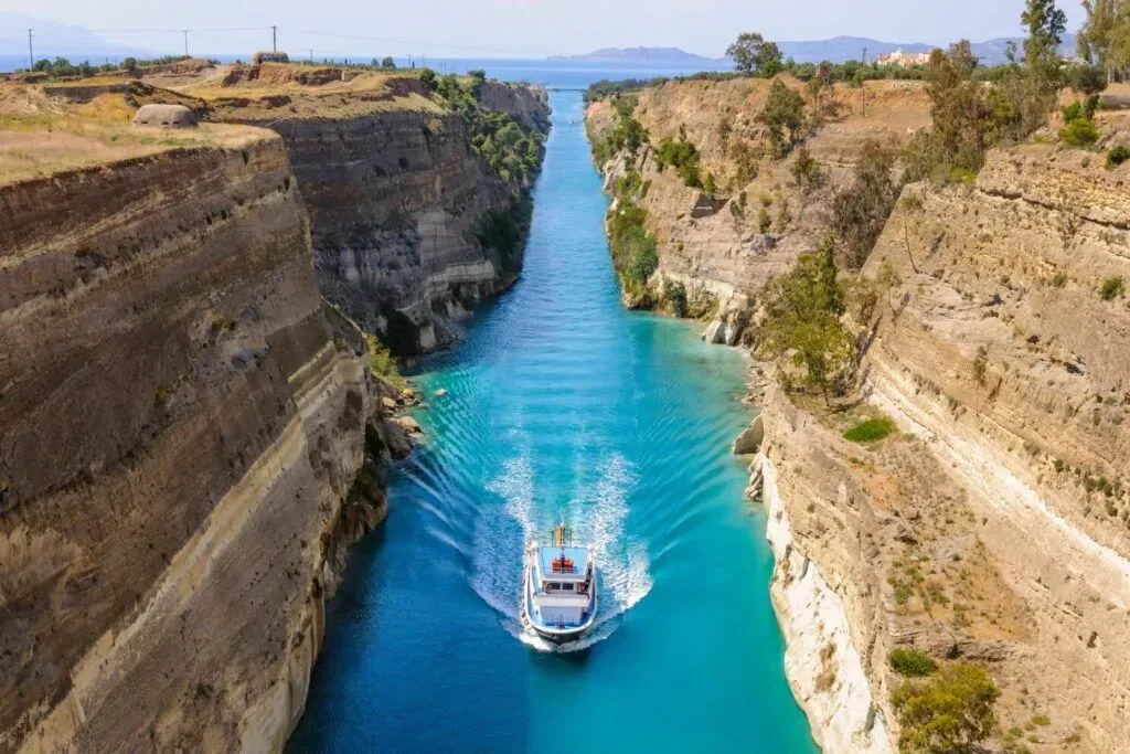 A blue canal with a boat passing through rocky cliffs under a clear sky.