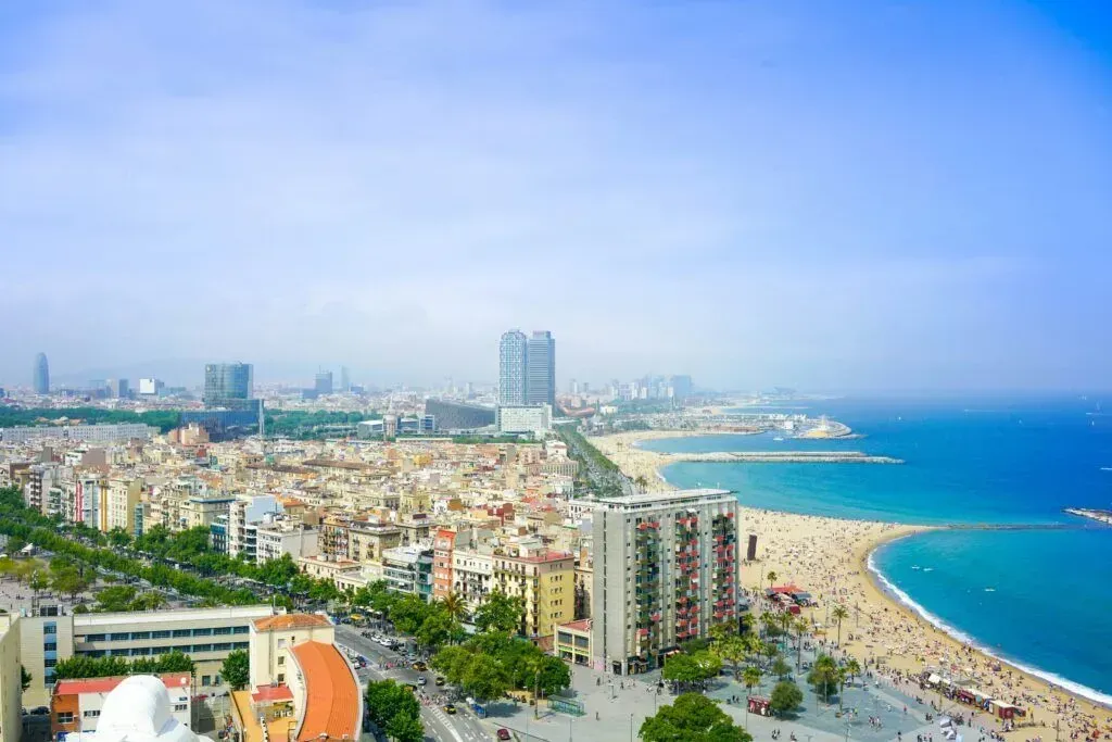 Aerial view of a coastal city with a sandy beach, blue sea, and dense buildings under a clear sky