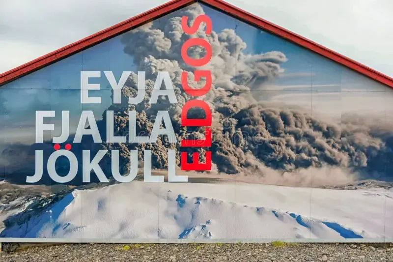 Sign on a building with Eyjafjallajökull in white text and ELDGOS in red over an erupting volcano scene