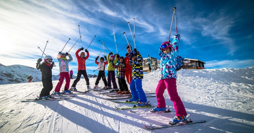 Group of skiers in colorful winter gear posing on a snowy mountain under a bright blue sky