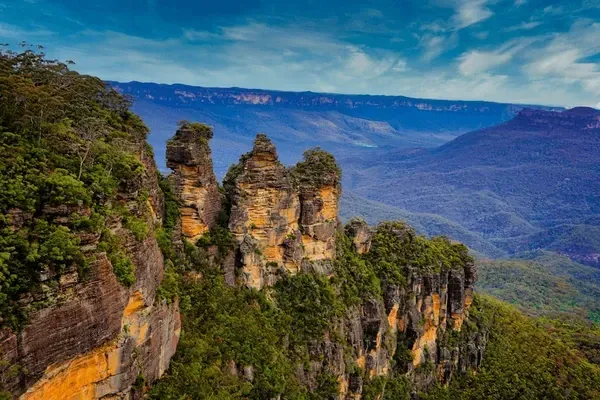 Jagged sandstone cliffs above a green valley under a blue sky