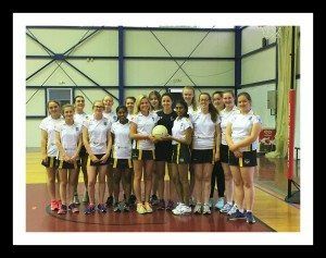 Volleyball team posing indoors on a court, wearing white jerseys and holding a ball