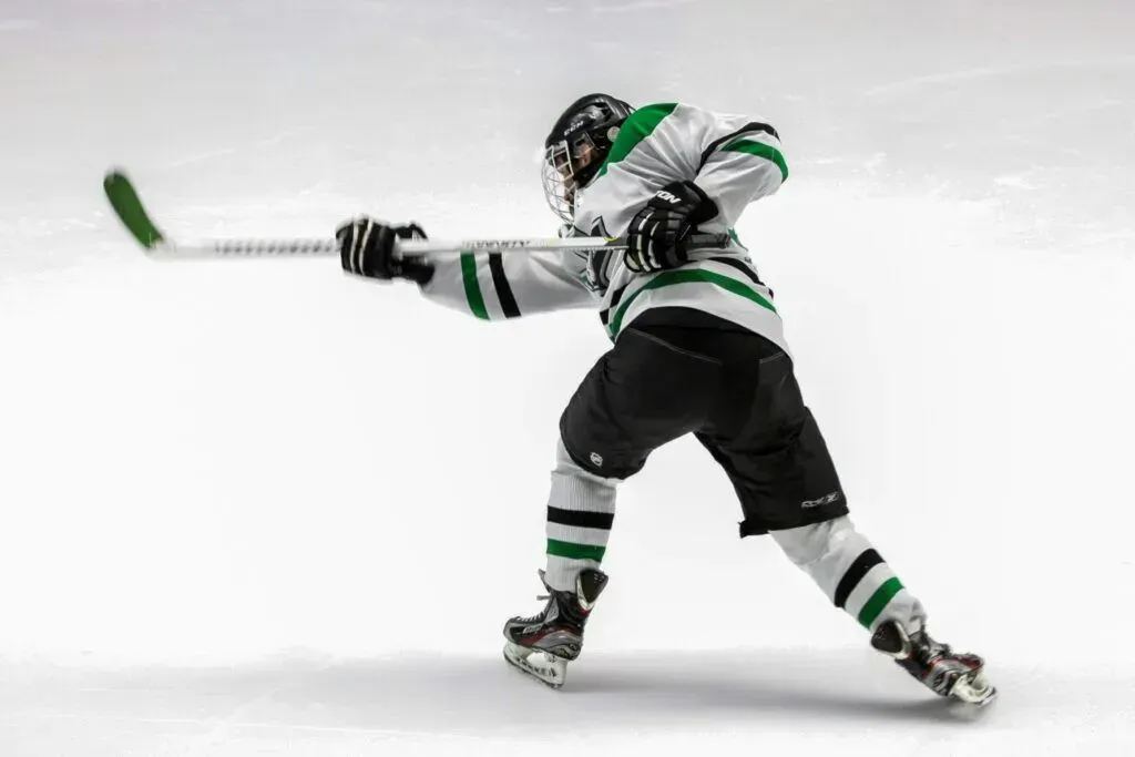 Hockey player in green and black uniform swinging a stick on ice, seen from behind