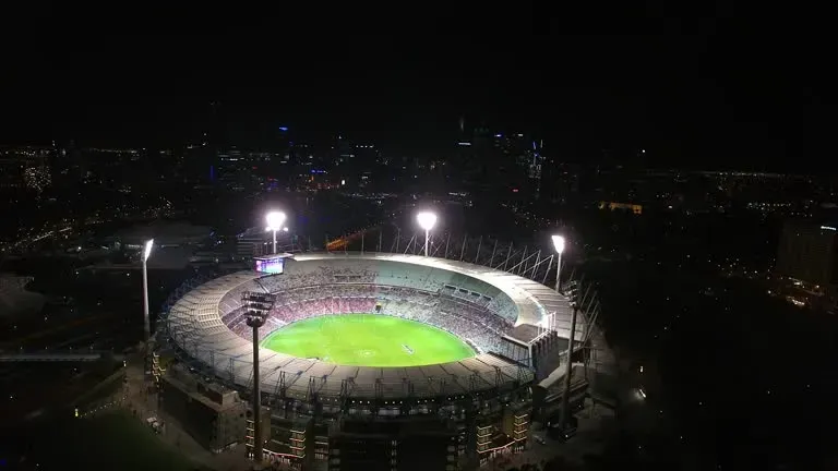 Floodlit baseball stadium at night, with bright green field and empty stands surrounding it.