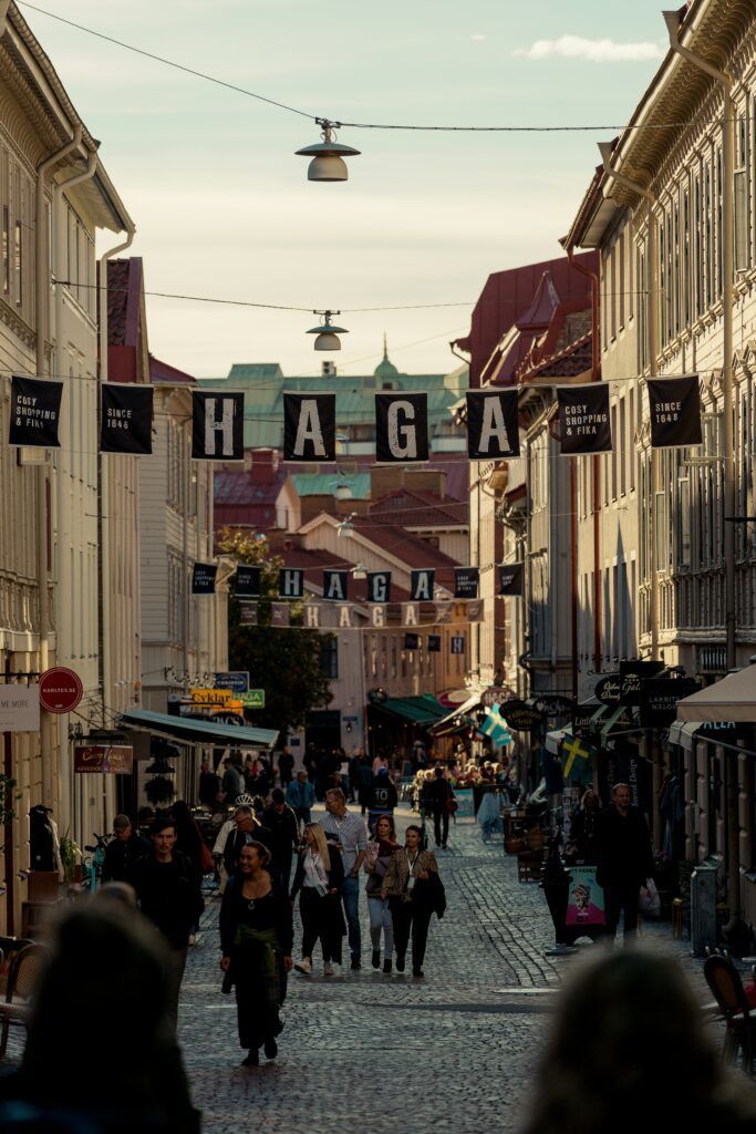 Crowded cobblestone street lined with buildings and hanging flags under a bright sky