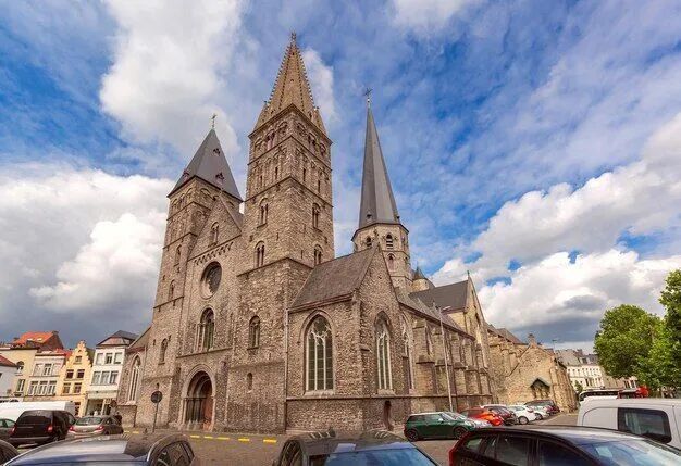 Stone church with tall spires on a street, under a partly cloudy sky