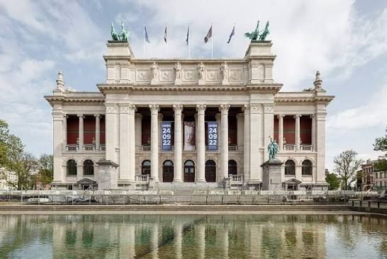 A grand neoclassical museum with columns and statues reflected in a calm lake