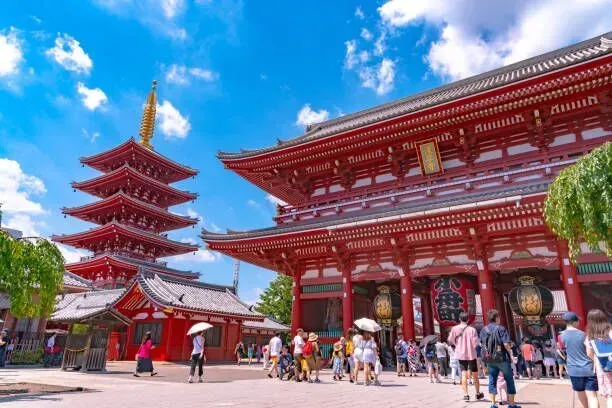 Red pagoda and temple gate in a sunny Japanese-style courtyard with visitors and blue sky