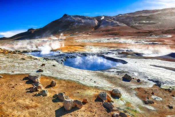 Steaming hot spring and rocky geothermal landscape under a blue sky