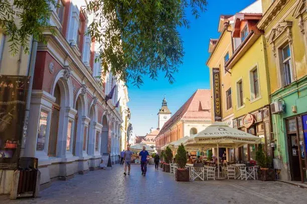 Colorful cobblestone street with pedestrians, cafés, and historic buildings under a bright blue sky