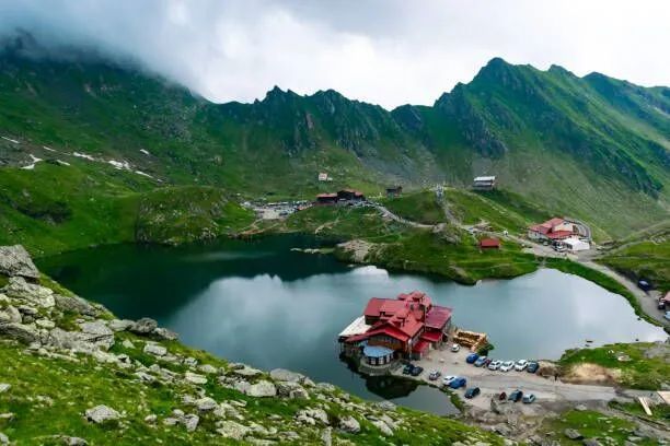 Mountain lake with green slopes, red-roof lodge, and small boats on the shore