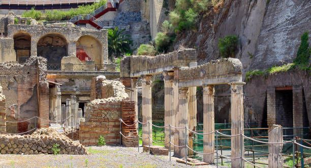 Ancient stone ruins with arches and columns built into a rocky cliff, with a walkway in front