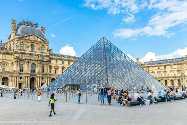Glass pyramid at the Louvre Museum courtyard with tourists and blue sky