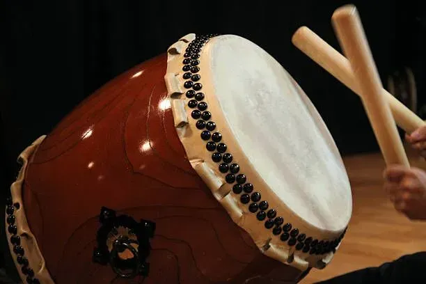 Close-up of a red taiko drum being struck with wooden drumsticks
