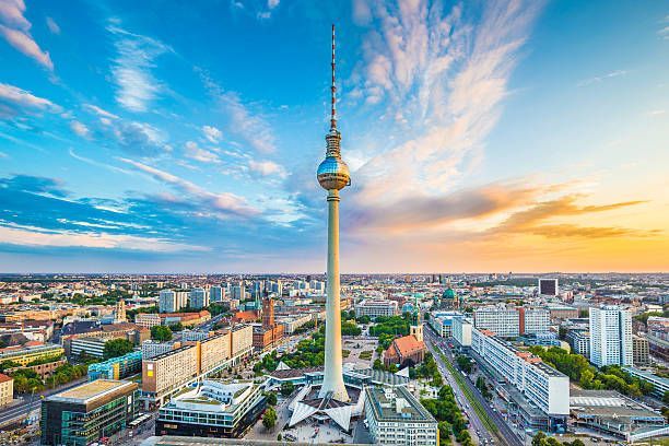 Berlin TV Tower rising over a city skyline at sunset, with colorful clouds and wide cityscape.