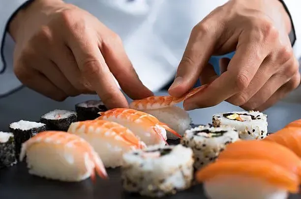 Hands arranging assorted sushi pieces on a plate at a table