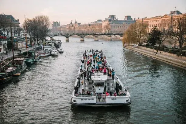 Tour boat crowded with passengers on a river between city buildings at sunset