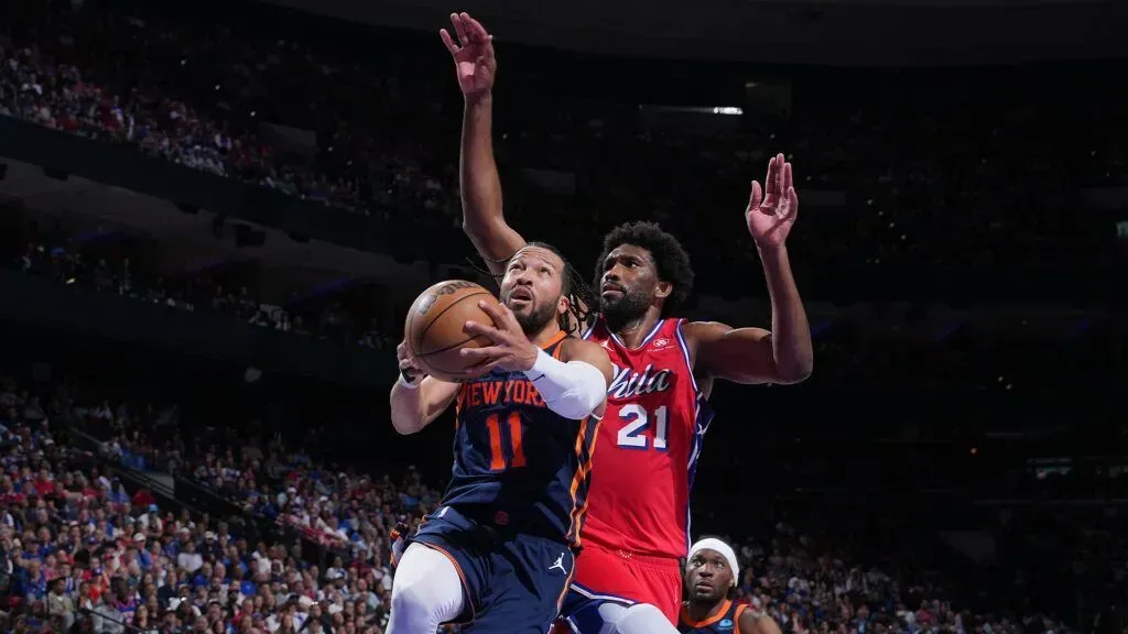 Basketball players in red and blue jerseys leap for a rebound in a crowded arena.