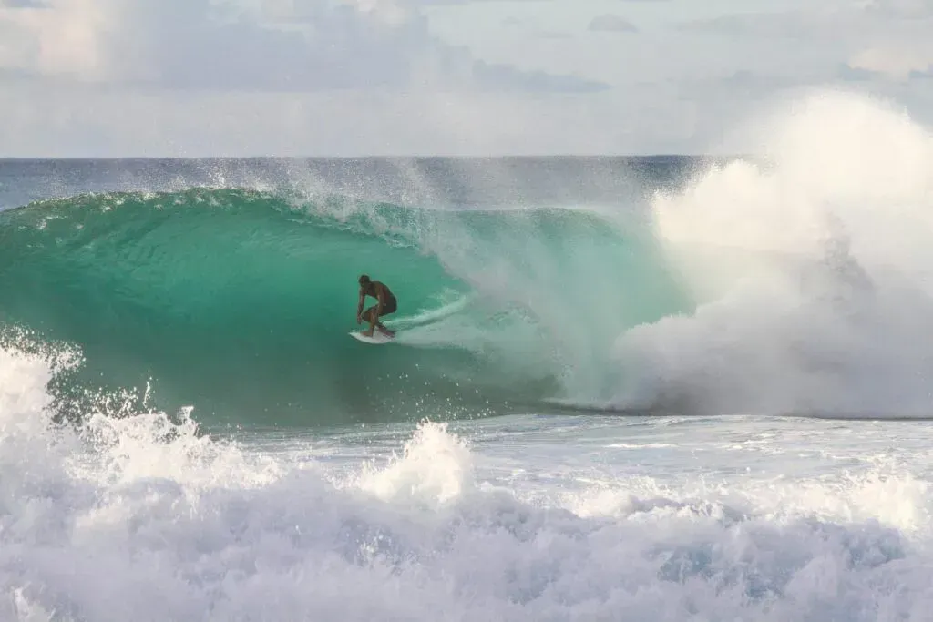 Surfer riding inside a turquoise wave with white spray crashing around them