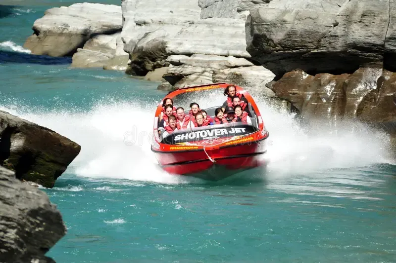 Red speedboat splashing through rocky whitewater with passengers onboard