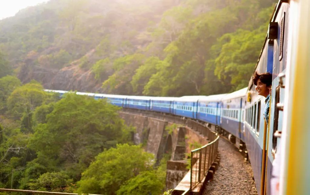 Blue train curving through a lush green mountainside in misty daylight