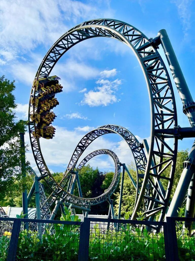 Roller coaster train hanging upside down on a looping steel track against a blue sky