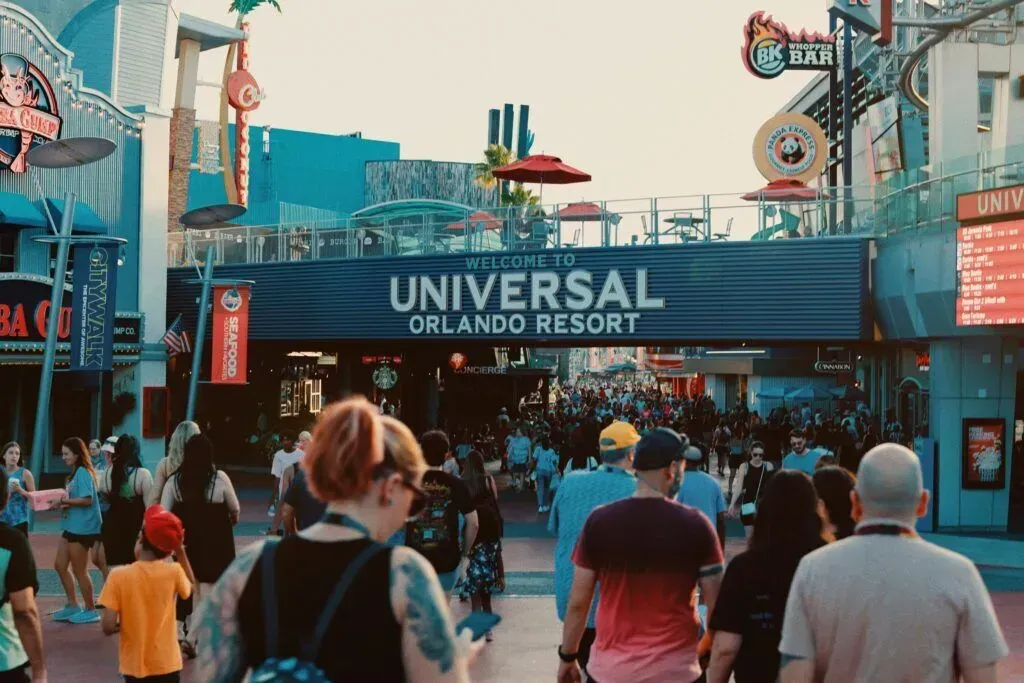 Crowd walking toward Universal Orlando Resort entrance under blue sign on a sunny day