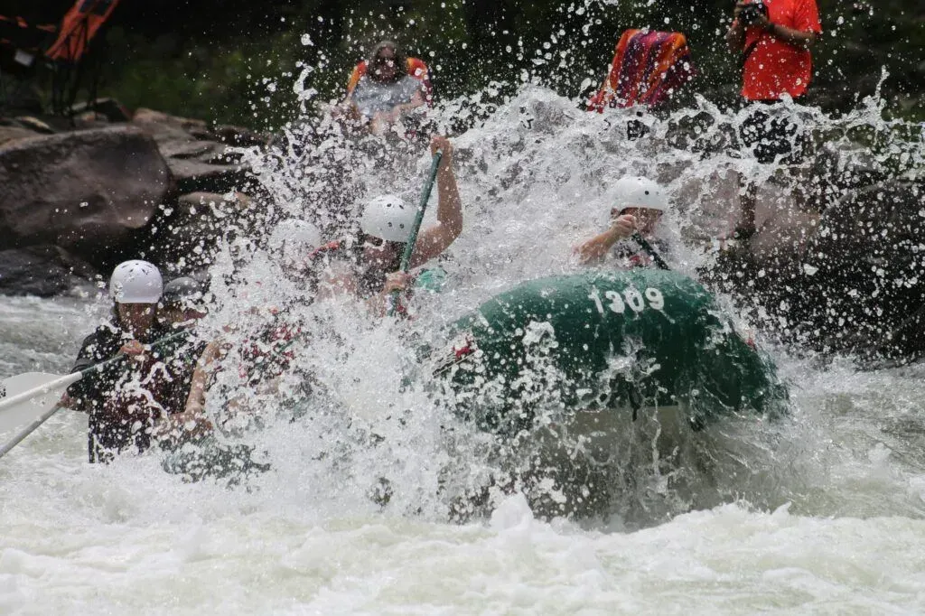 Whitewater rafters in green and black boats splash through rough rapids