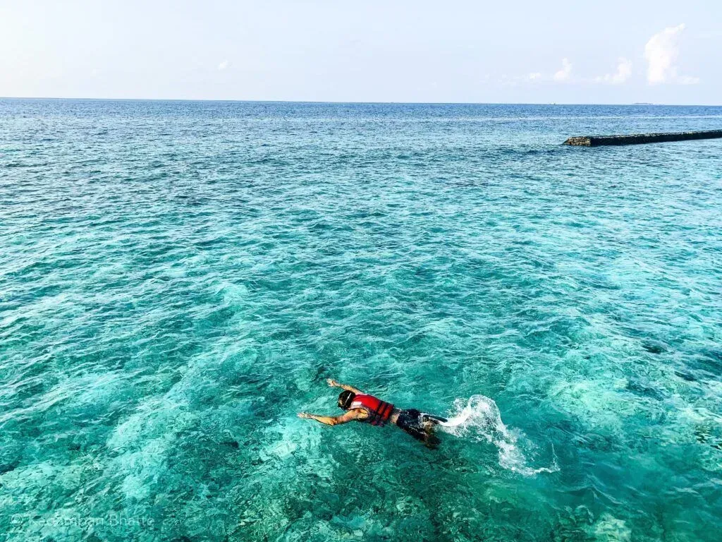 Swimmer in red swimsuit floating in clear turquoise ocean under a bright sky
