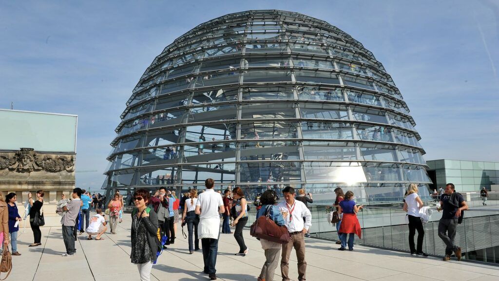 People walking toward the glass dome of the Reichstag building under a clear sky