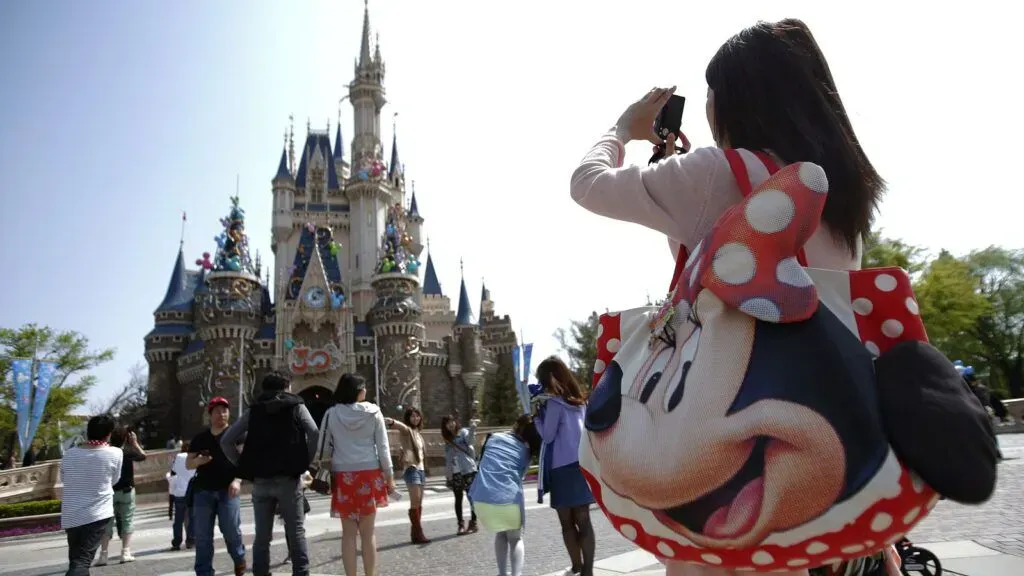 Minnie Mouse character posing before a fairytale castle with visitors in a theme park