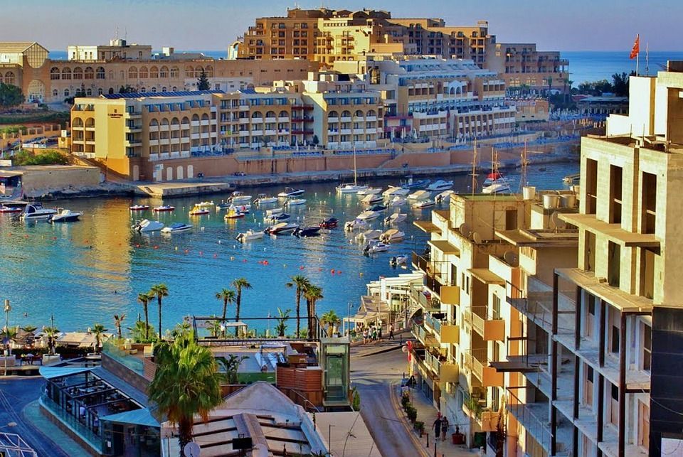 Harbor cityscape with boats, palm trees, and sunlit buildings along the waterfront