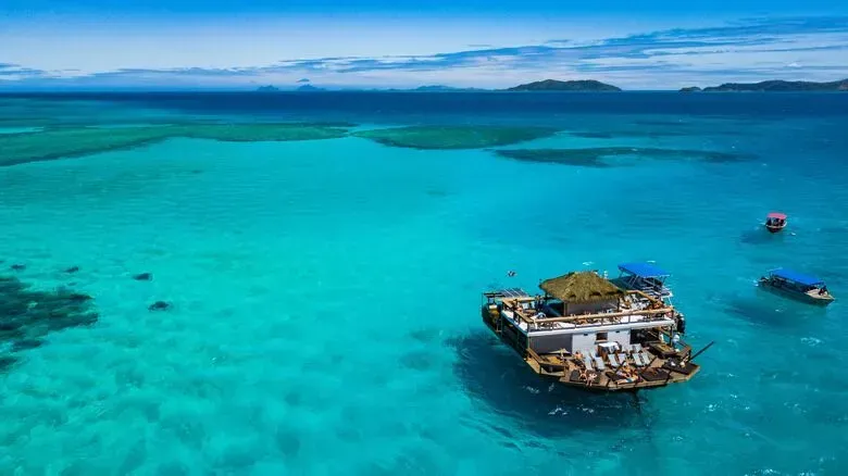 Turquoise ocean with a small hut-covered boat floating near a tropical shoreline