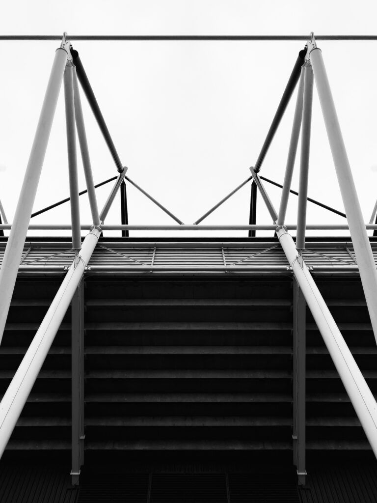 Black-and-white view of stadium stairs and steel support beams under a modern canopy