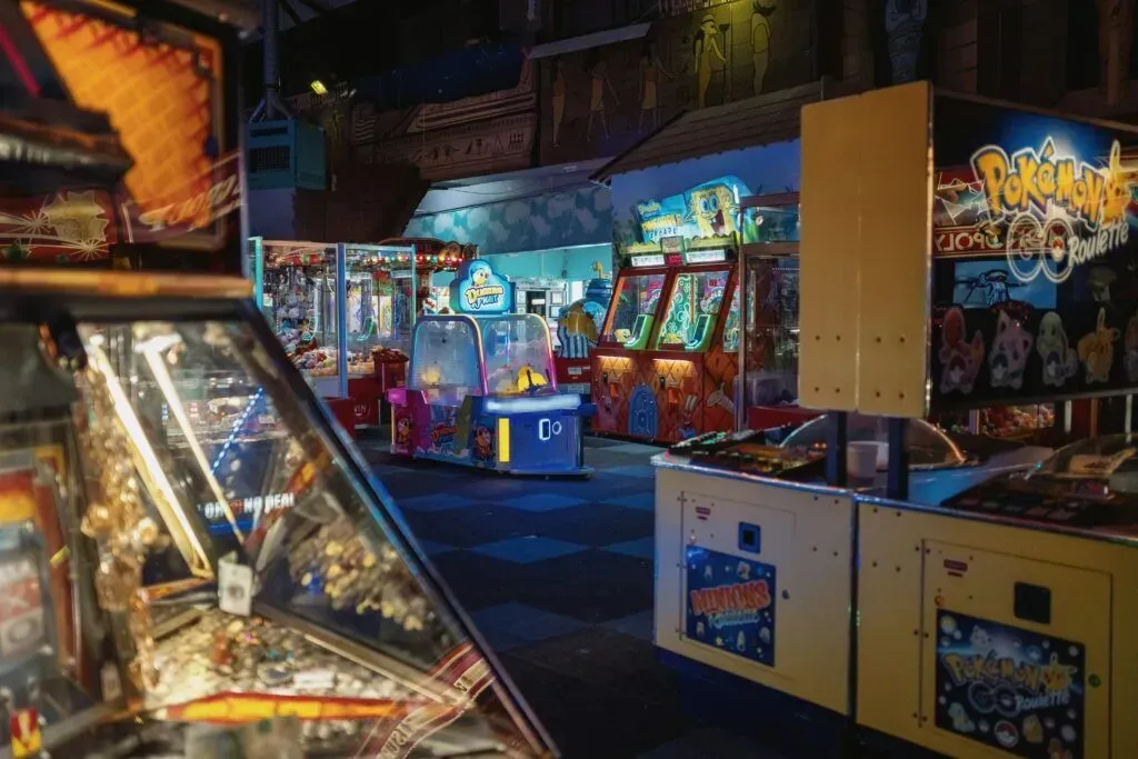 Neon-lit arcade with rows of pinball and arcade machines in a dim indoor entertainment venue
