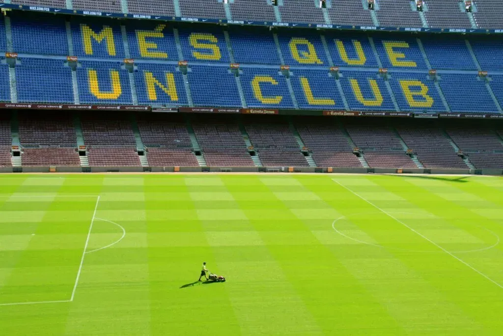 Empty soccer stadium with blue seats spelling “MES QUE UN CLUB” and a mower on the field