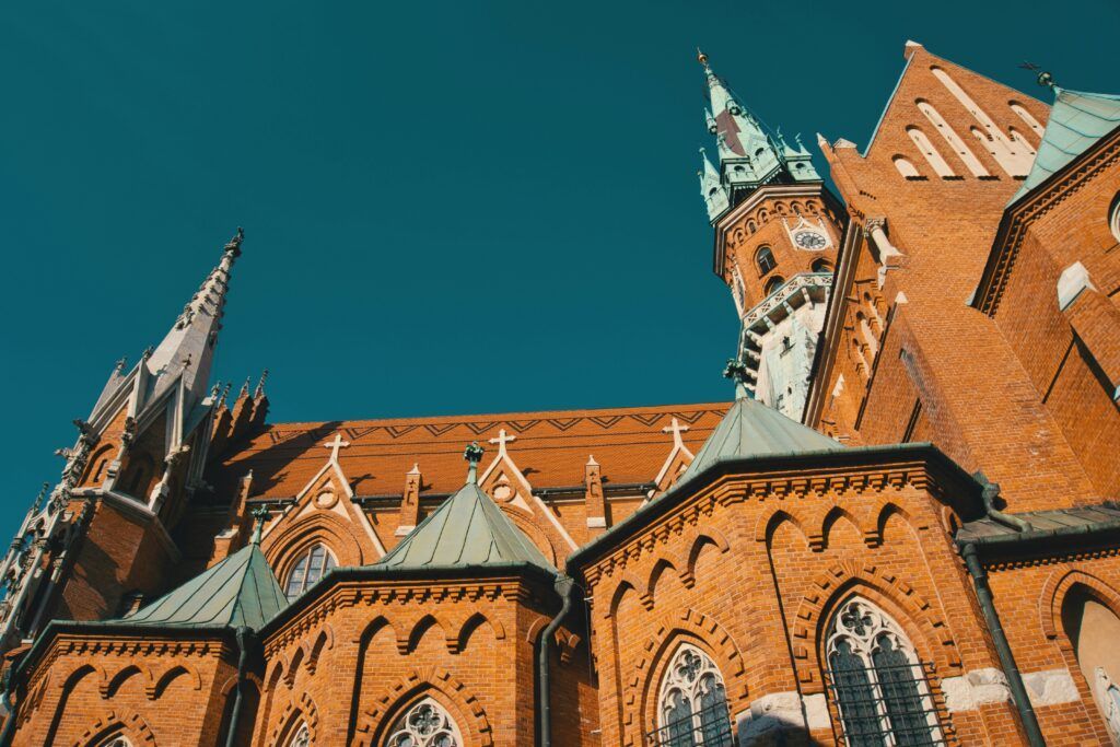 Red-brick Gothic building with ornate towers and pointed spires against a blue sky