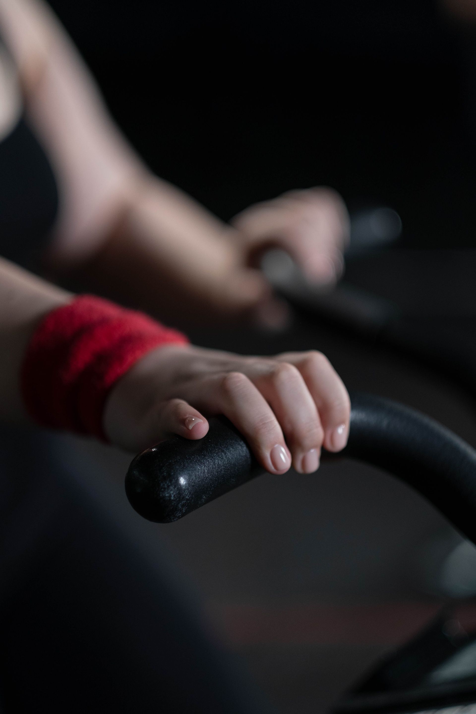 Hands gripping black exercise handlebars with a red wristband in a dim gym setting