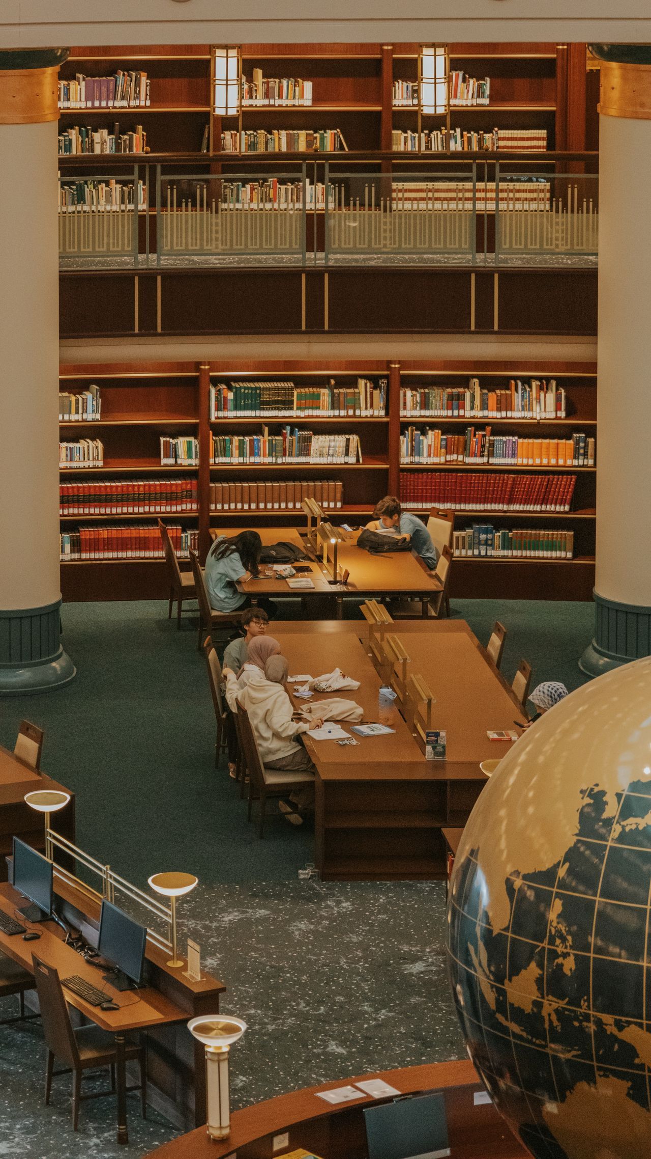Library with tall bookshelves, reading tables, and a large globe in the foreground