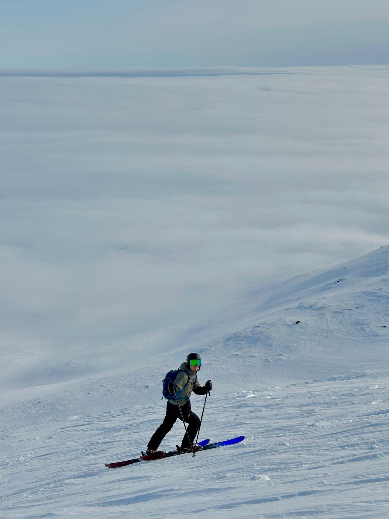 Skier in a green helmet descends a snowy slope with blue skies above