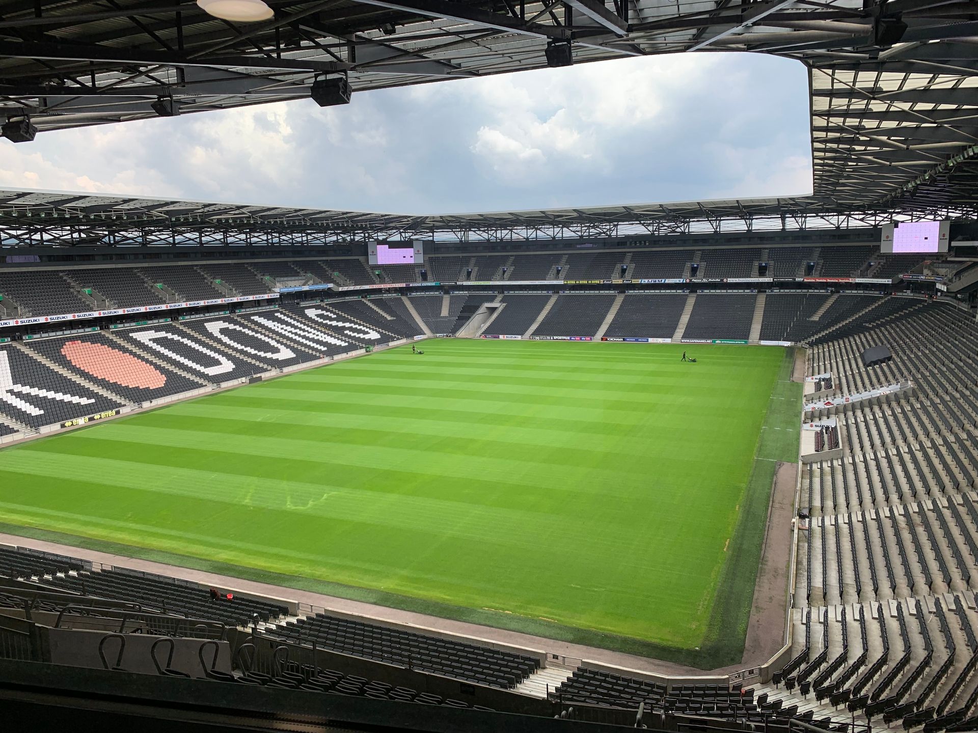 Empty soccer stadium with a green field and black-and-white seating under a partially covered roof