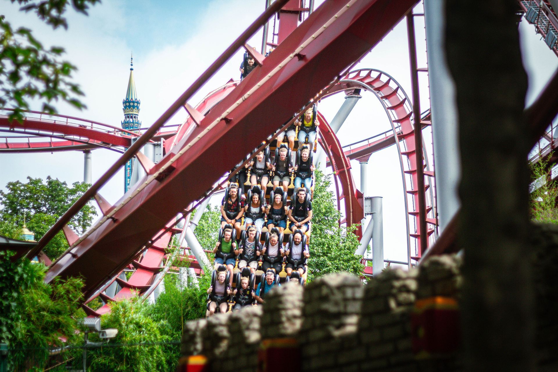 A roller coaster train full of riders twists through a red track in a green park.