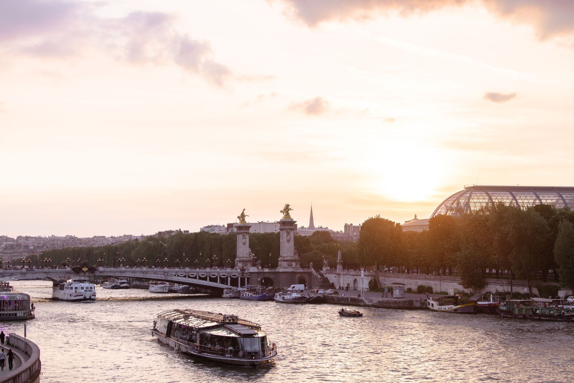 Sunset over a river with boats, bridges, and a skyline glowing in warm light